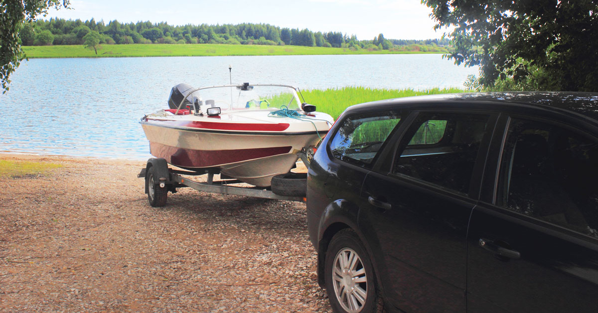 A car reversing with boat trailer to a shore.