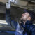 An A‑Katsastus inspector examines the underside of the car with a flashlight.